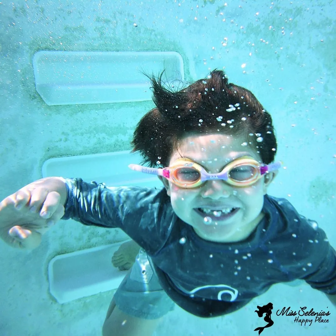 A young swimmer smiling underwater during a lesson